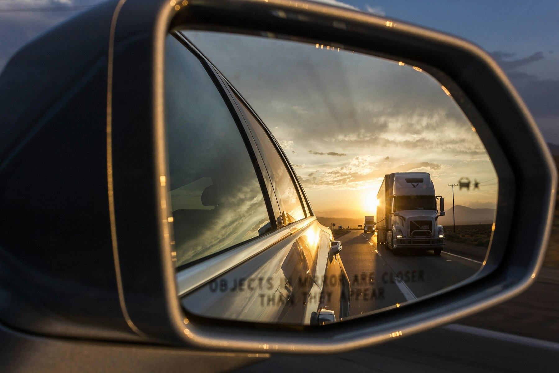 Semi truck reflected in a side mirror on the highway at sunset