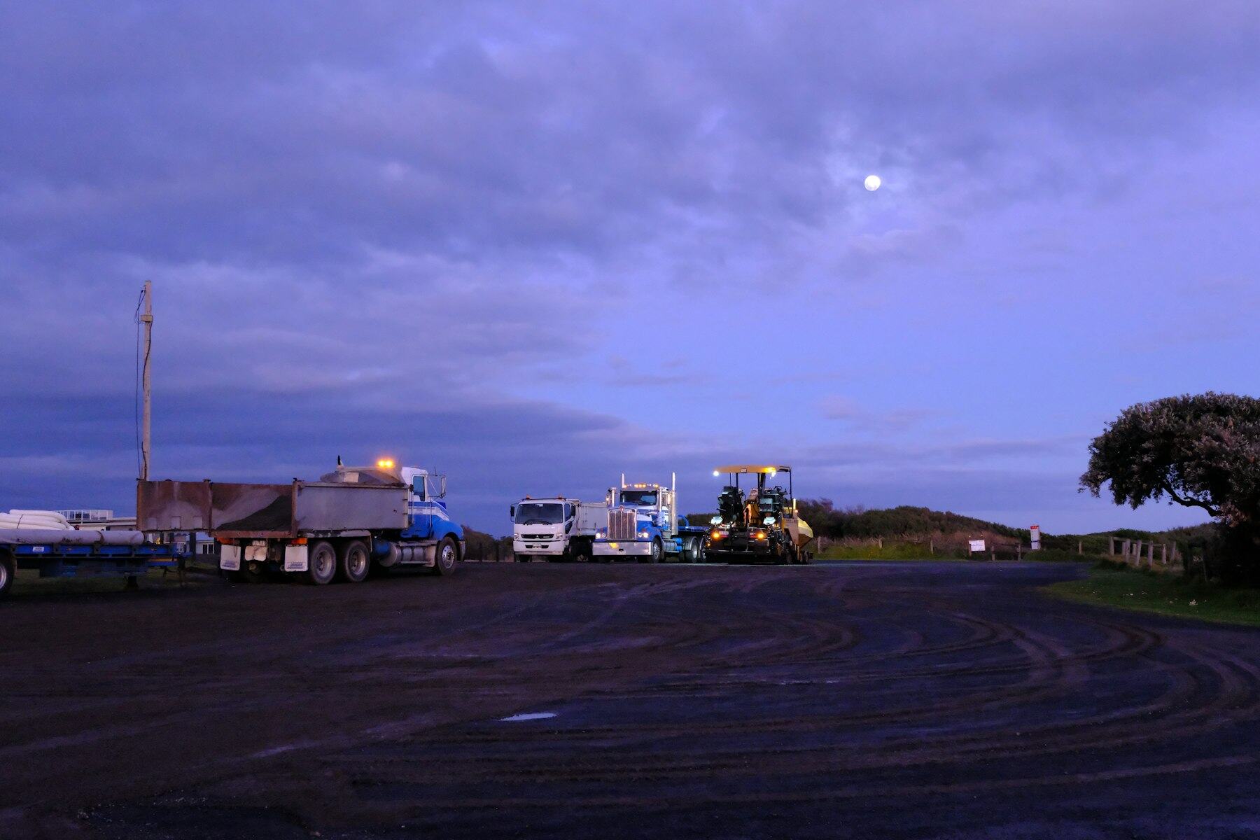 Tractor-trailers parked in a yard under a deep blue dusk sky